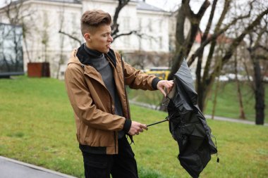 Kırık şemsiyeli bir adam açık havada yağmur altında rüzgarla savaşıyor.