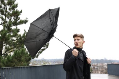 Kırık şemsiyeli bir adam açık havada yağmur altında rüzgarla savaşıyor.