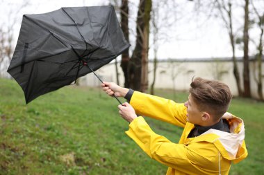 Kırık şemsiyeli bir adam açık havada yağmur altında rüzgarla savaşıyor.