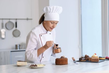 Mutfaktaki masada erimiş çikolatayla pasta süsleyen kıdemli pasta şefi