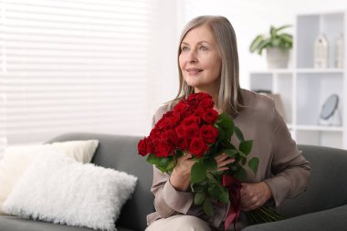Evdeki kanepede gül buketiyle gülümseyen kadın.