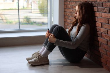 Evdeki tuğla duvarın yanındaki üzgün genç kız.