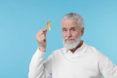 Çoklu Skleroz farkındalığı. Açık mavi arka planda turuncu kurdeleli son sınıf öğrencisi.