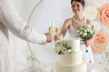 Mutlu evli çiftler masada kadeh tokuşturuyor. Düğün pastası içeride, seçici bir odak noktası var.