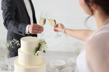 Evde düğün pastası olan evli bir çift şampanya bardaklarını tokuşturuyor.
