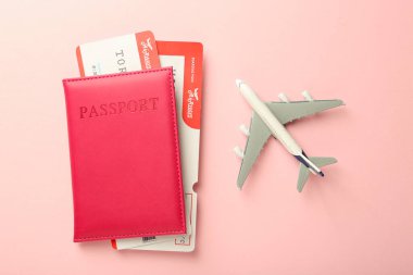 Biletli pasaport ve pembe arka planda uçak modeli.