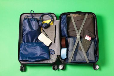 Elbiseli bavul, akıllı telefon ve açık yeşil arka planda diğer eşyalar, üst görünüm