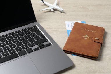 Pasaport, uçuş bileti, uçak modeli ve laptop ahşap masada, yakın plan.