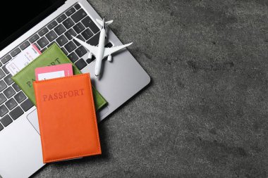 Pasaportlar, uçuş biletleri, uçak modeli ve laptop gri masada, üst manzara. Metin için boşluk