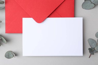 Boş tebrik kartı, kağıt zarf ve okaliptüs yaprakları açık gri arka planda, düz yatıyordu.