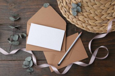 Boş tebrik kartı, kağıt zarflar, okaliptüs yaprakları, tahta masa üzerinde kurşun kalem ve kurdele.