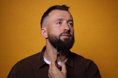 Turuncu arka planda makasla sakal kesen adam.