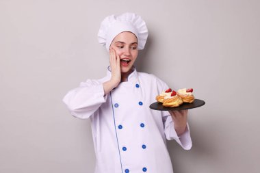 Üniformalı şekerci açık gri arka planda lezzetli profiteroller tutuyor.