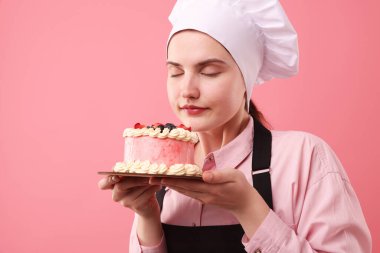 Şekerci pembe arkaplanda lezzetli bir pasta tutuyor, mesaj için yer var.
