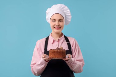 Açık mavi arka planda lezzetli çikolatalı pasta yapan bir pastacı.