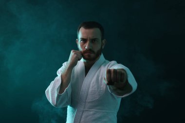 Üniformalı bir adam renkli ışıklarla ve dumanla karate yapıyor.