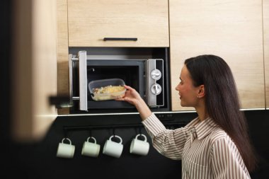 Kadın, yemeğiyle birlikte mikrodalgayı içine koyuyor.
