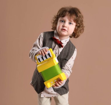 Kahverengi arka planda oyuncak akordeon çalan sevimli küçük çocuk.