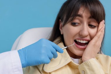 Korkak kadının açık mavi arka planda dişçiyle randevusu var.