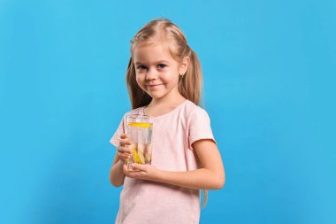 Açık mavi arka planda bir bardak limonata olan kız. Tazeleyici içecek.