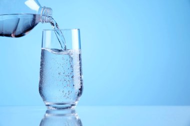 Açık mavi arka planda şişeden bardağa ferahlatıcı soda dökülüyor, yakın plan. Metin için boşluk