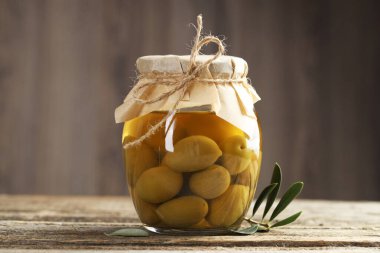 Cam kavanozda turşulu yeşil zeytin ve ahşap masada yapraklar, yakın plan.