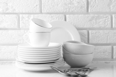 Different clean dishware on white table near brick wall