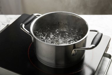 Kaynar suyla tencereyi pişirmek ve arka plandaki gri ışığa karşı soba, yakın plan