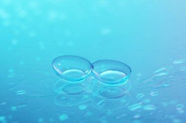 Açık mavi ayna yüzeyine bir çift kontak lens ve su damlası, yakın plan.