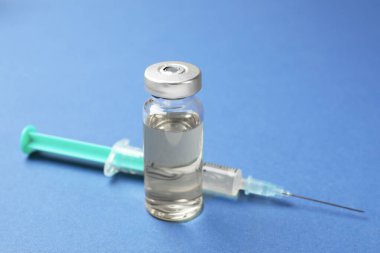Cam şişede Hepatit aşısı ve mavi arka planda şırınga, yakın plan.