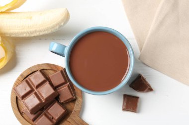 Lezzetli çikolatalı süt, parçalar ve muz beyaz ahşap masada, düz uzanmış