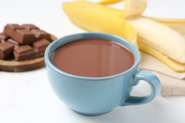 Lezzetli çikolatalı süt, parçalar ve muz beyaz masada, yakın plan.