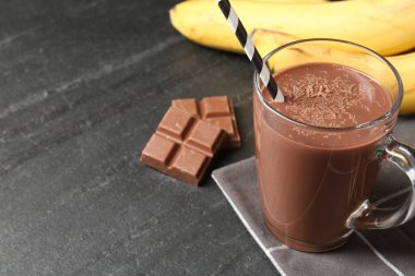 Cam bardakta lezzetli çikolatalı süt, siyah masada parçalar ve muzlar, yakın plan. Metin için boşluk