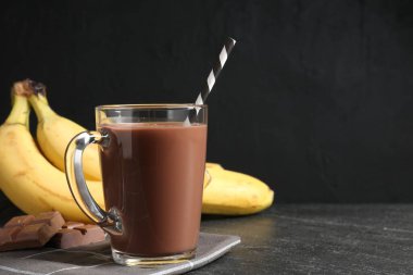 Cam bardakta çikolatalı süt, siyah masada parçalar ve muzlar, metin için yer