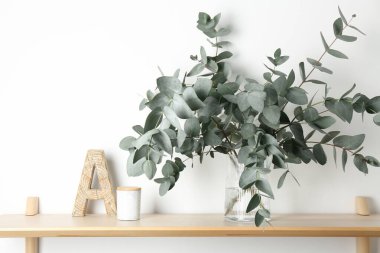 Vazodaki okaliptüs dalları ve beyaz duvarın yanındaki ahşap masa üzerindeki diğer dekorlar.