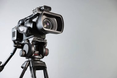 Açık gri arkaplanda tripodu olan modern video kamera, metin için boşluk