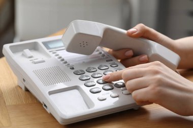 Kadın ahşap masadaki telefon numarasını bulanık arkaplana karşı çeviriyor.