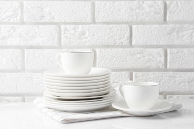 Tuğla duvarın yanındaki beyaz masada farklı temiz bulaşık takımları. Metin için boşluk