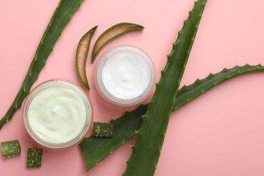 Aloe vera özütüyle nemlendirici krem ve pembe arkaplanda yapraklar, düz bir zemin.