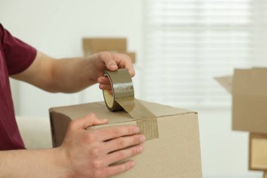 Kapalı alanda yapıştırıcı bantlı karton kutu mühürleyen adam.