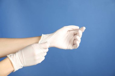 Doktor mavi arka plana tıbbi eldiven takıyor, yakın plan.