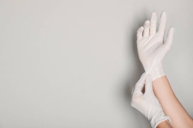 Doktor açık gri arka plana tıbbi eldiven takıyor, yakın plan. Metin için boşluk