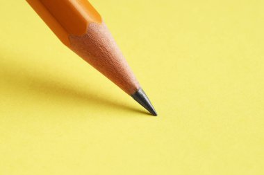 Sarı arka planda keskin bir grafit kalem, yakın plan.