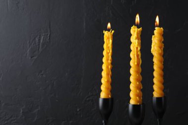 Balmumu mumlarını siyah arka planda şamdanlarla yakmak, yakın plan. Metin için boşluk