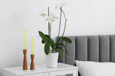 Yanan mumlarla süslü şamdanlar ve yatağın yanındaki komodinin yanında orkide çiçeği.