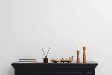 Beyaz duvarın yanındaki şöminede yanan mumlar ve diğer dekorlarla süslü şamdanlar.