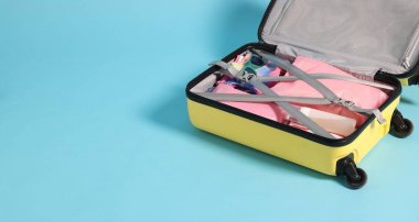 Açık mavi arkaplanda giysiler ve diğer eşyaların olduğu bavul, metin için boşluk