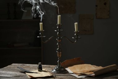 Şamdandaki mumlar, eski kağıtlar, mürekkep hokkası ve tüy kapalı masa üzerinde.