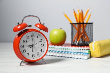 Alarm saati, kırtasiye malzemesi ve beyaz ahşap masada elma. Bilgi zamanı