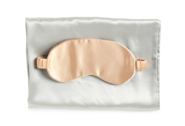 Beyaz arka planda ipek çarşaflar ve uyku maskesi, üst manzara.